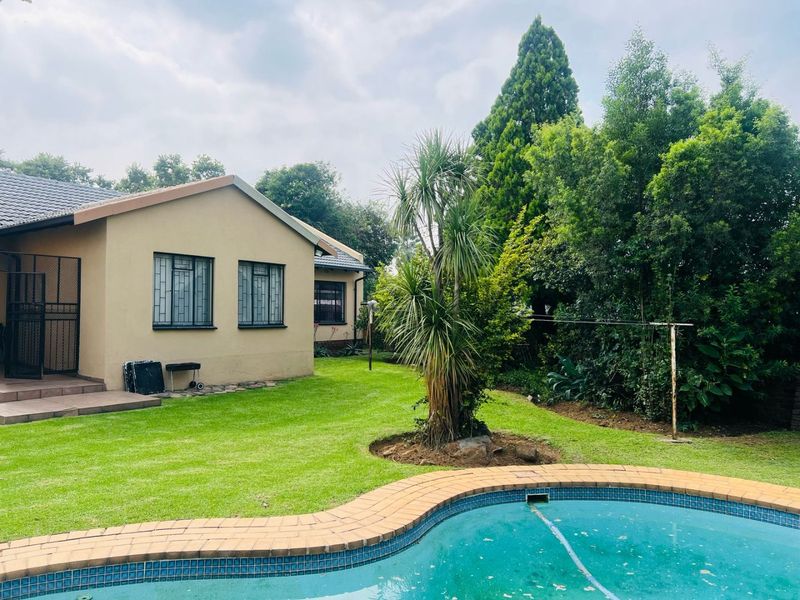 Rear view of the property featuring a well-maintained lawn, a swimming pool with tiled coping, and security bars on the windows.