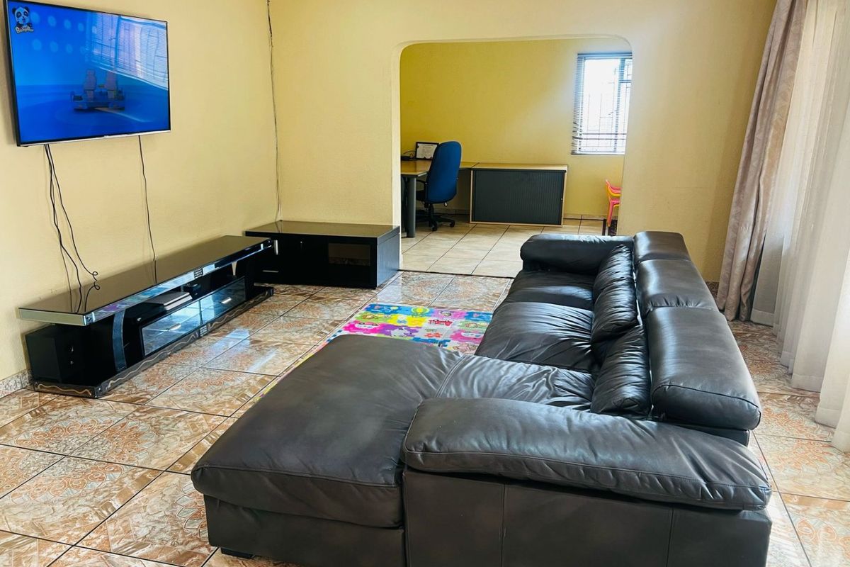 A living room featuring tiled flooring and an arched opening leading to an adjacent office or study area.