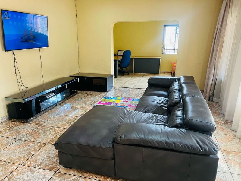 A living room featuring tiled flooring and an arched opening leading to an adjacent office or study area.