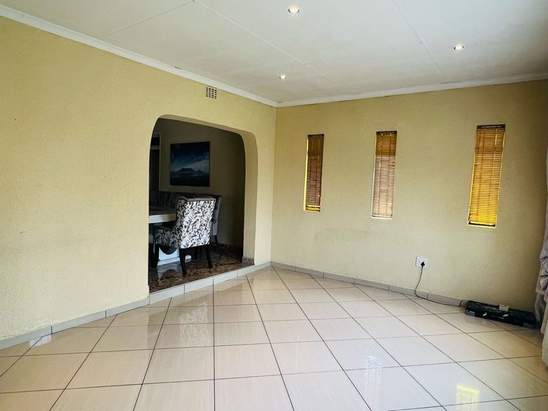 A spacious living area featuring neutral tiled flooring, recessed downlighting, and an arched transition leading to an adjacent dining space.