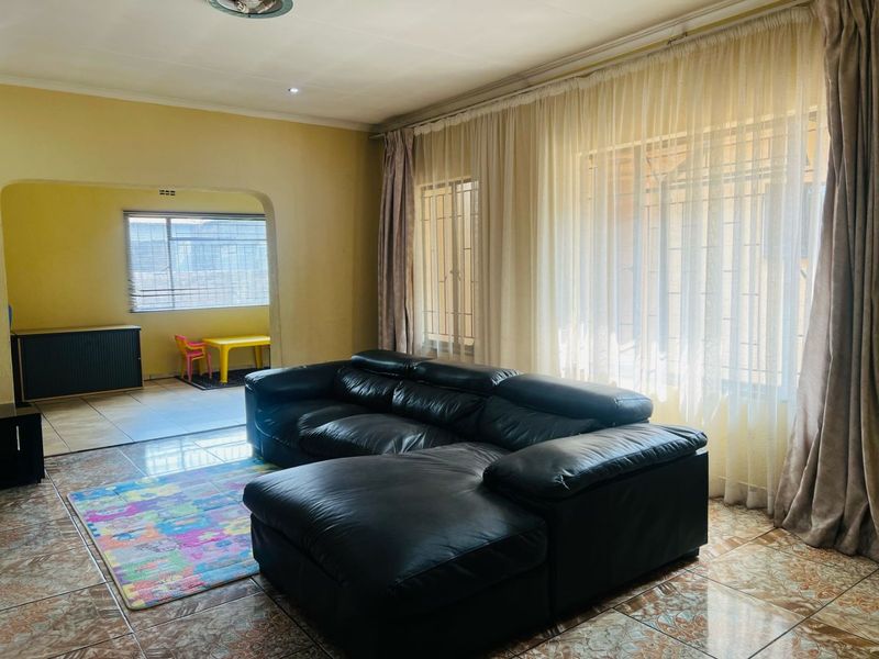 A spacious living area featuring tiled flooring and large windows with security bars, offering a bright and functional layout.