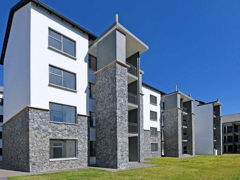 Modern apartment complex featuring stone cladding, white rendered walls, and private balconies with metal railings set against a clear blue sky.