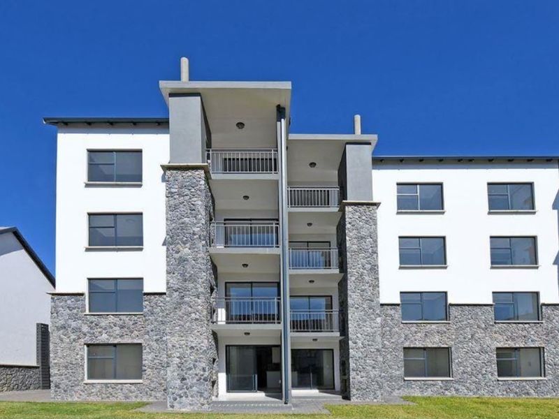 A modern apartment building facade featuring stone cladding, multiple balconies with metal railings, and large sliding glass doors.