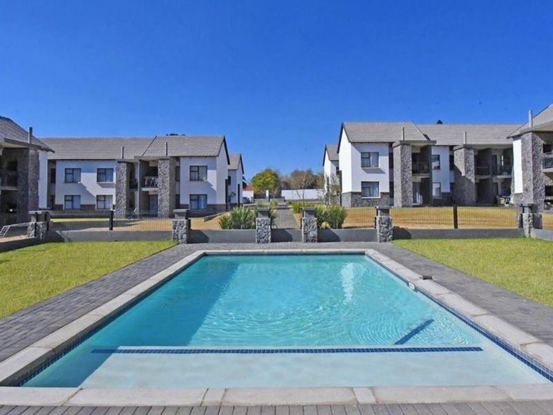 A well-maintained communal swimming pool area set within a modern apartment complex, featuring stone-clad architectural details and landscaped grounds.