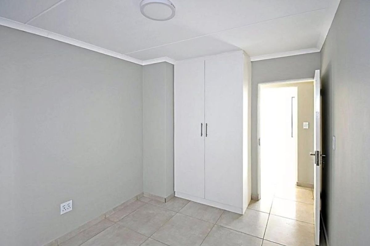A clean, empty bedroom featuring neutral grey walls, tiled flooring, and a built-in white wardrobe, offering a versatile space ready for personalization.