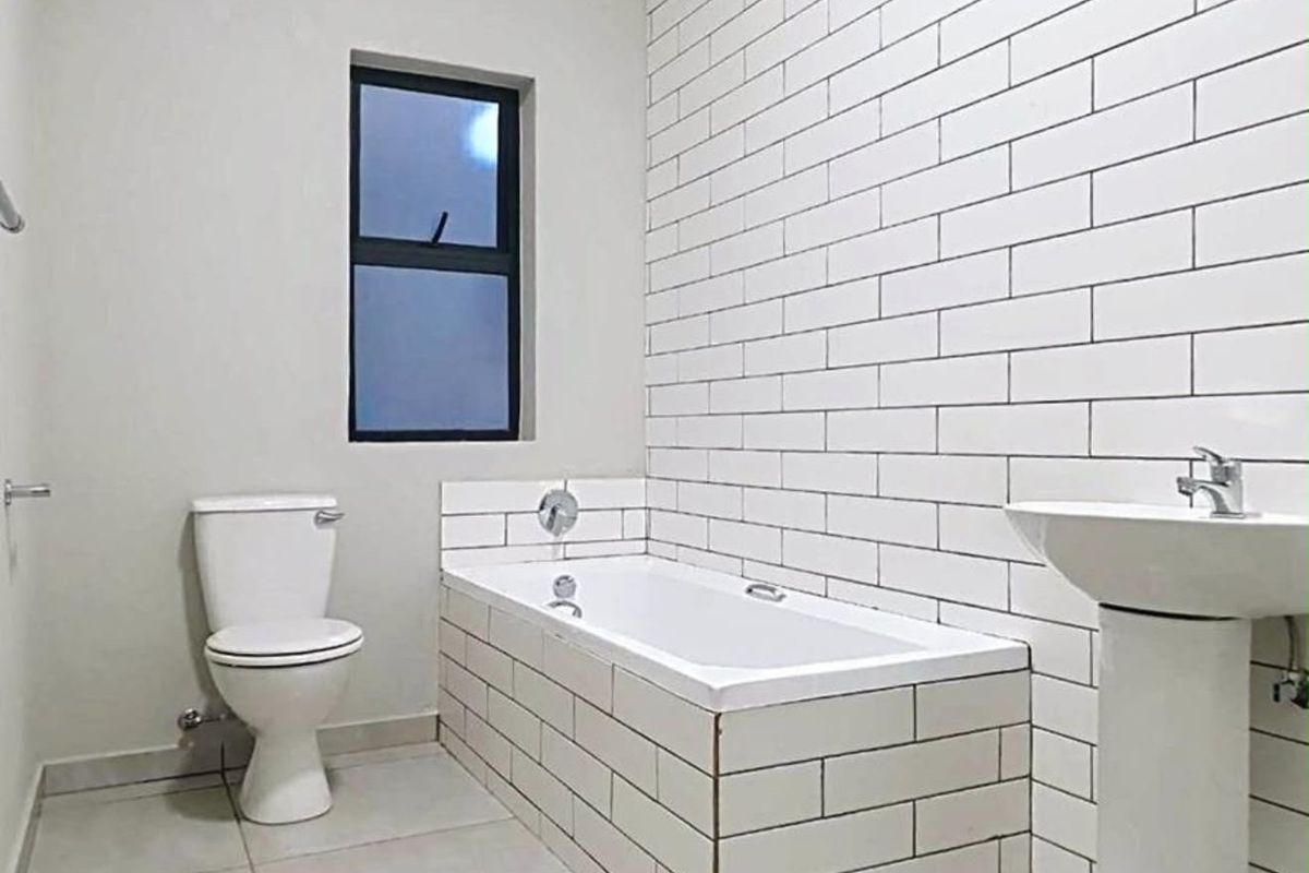 A clean, modern bathroom featuring a white bathtub with subway tile surround, a pedestal basin, and a standard toilet.