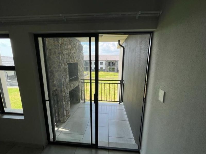 A covered balcony featuring tiled flooring, a built-in stone braai, and a metal balustrade, accessible via a sliding glass door.