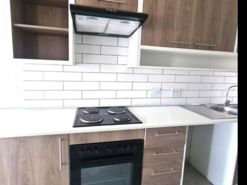 Modern kitchen featuring wood-finish cabinetry, white subway tile backsplash, integrated electric hob and oven, and a clean stone countertop.