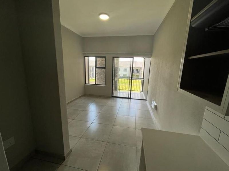 An open-plan living area featuring neutral tiled flooring, modern aluminium window frames, and a sliding door leading to an outdoor balcony space.