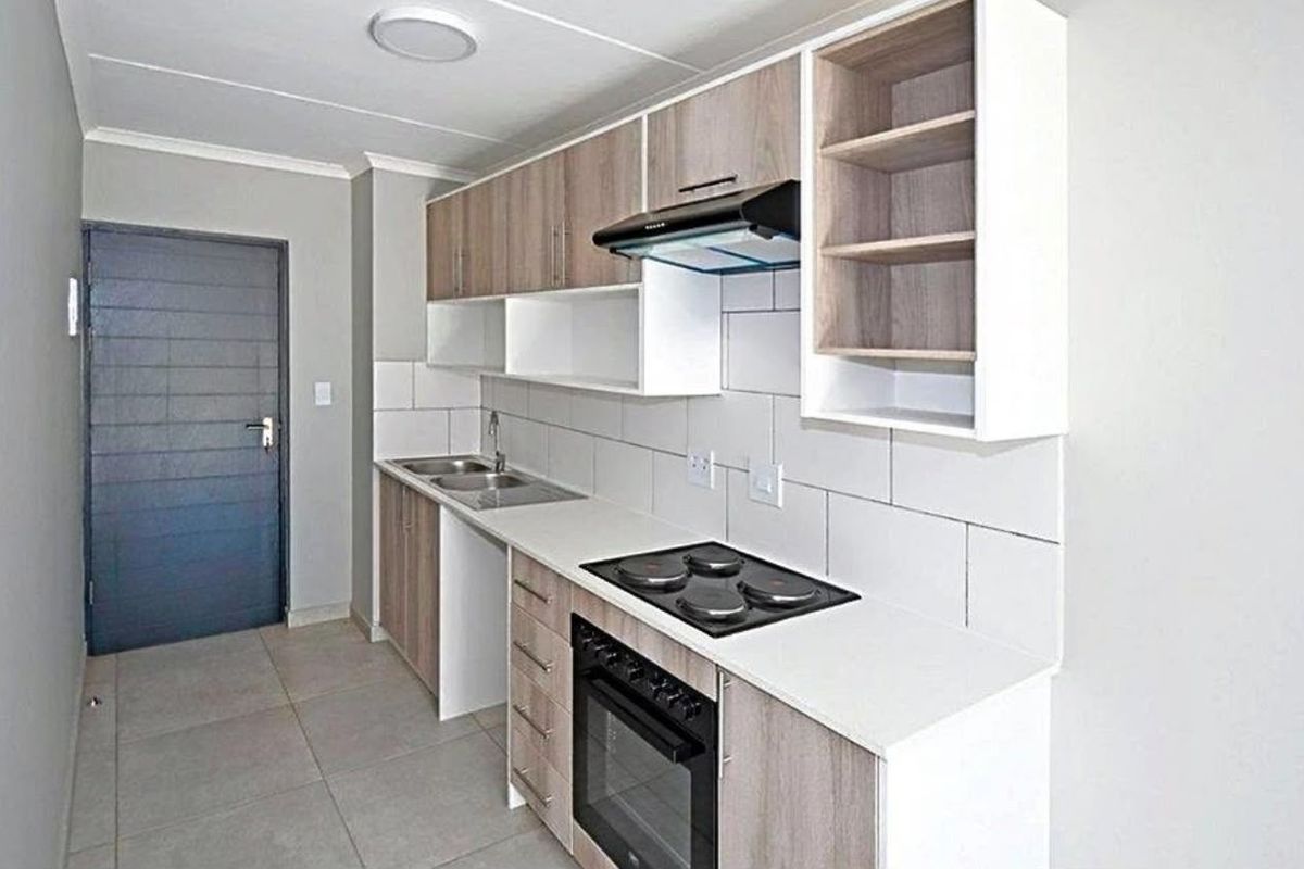 Modern kitchen featuring light wood-tone cabinetry, white countertops, a built-in oven with electric hob, extractor fan, and neutral tiled flooring.