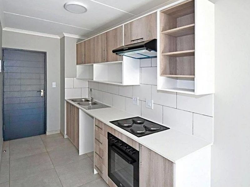 Modern kitchen featuring light wood-tone cabinetry, white countertops, a built-in oven with electric hob, extractor fan, and neutral tiled flooring.