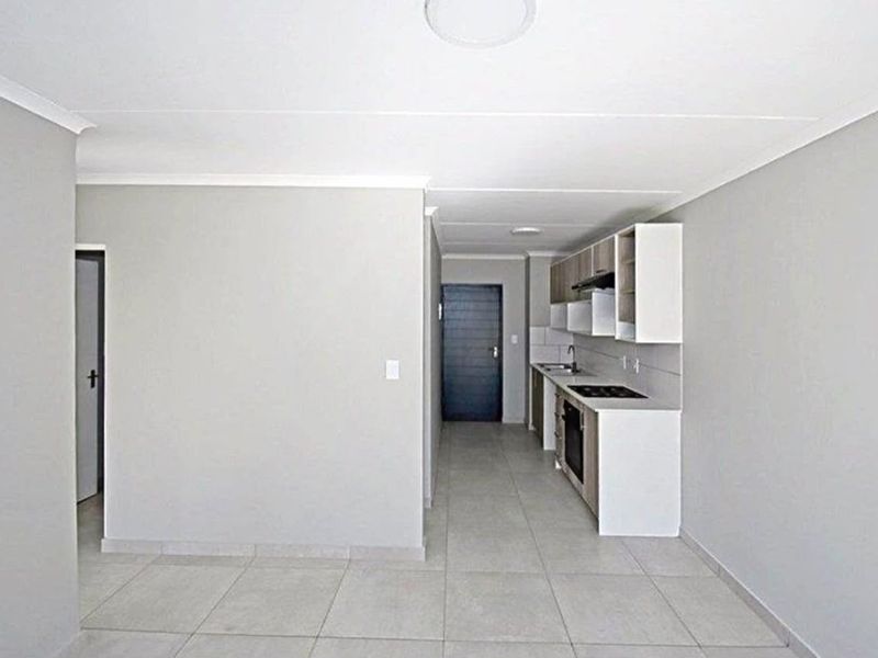 An open-plan living and kitchen area featuring modern cabinetry, built-in oven and hob, and neutral tiled flooring throughout.