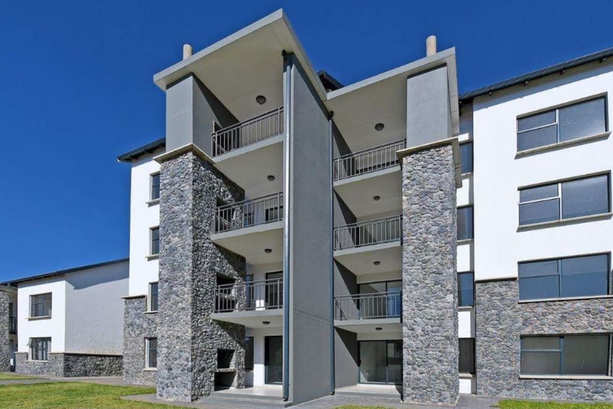 Modern apartment building exterior featuring stone cladding, multiple balconies with metal railings, and integrated built-in braai facilities on the ground level.