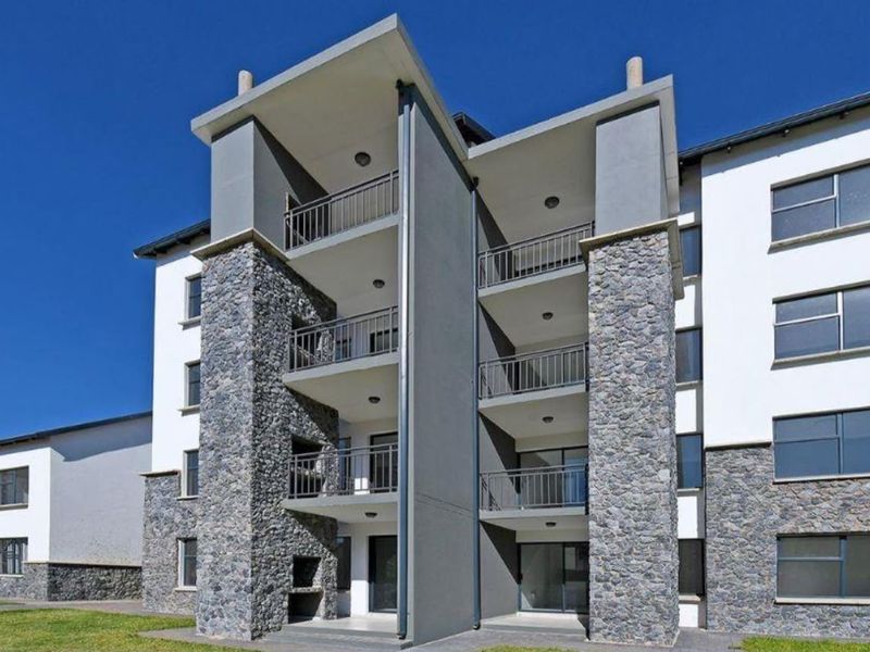 Modern apartment building exterior featuring stone cladding, multiple balconies with metal railings, and integrated built-in braai facilities on the ground level.
