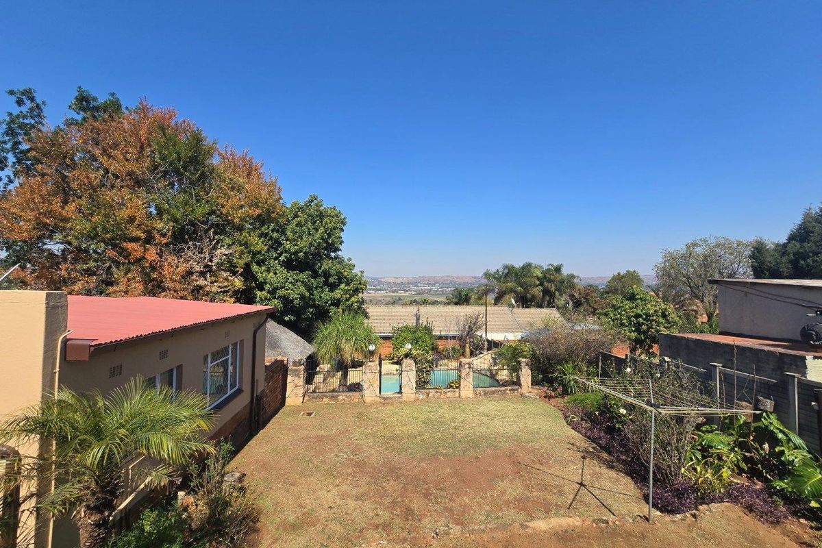 Elevated view of the rear garden featuring a swimming pool, lawn area, and surrounding residential properties with distant landscape views.