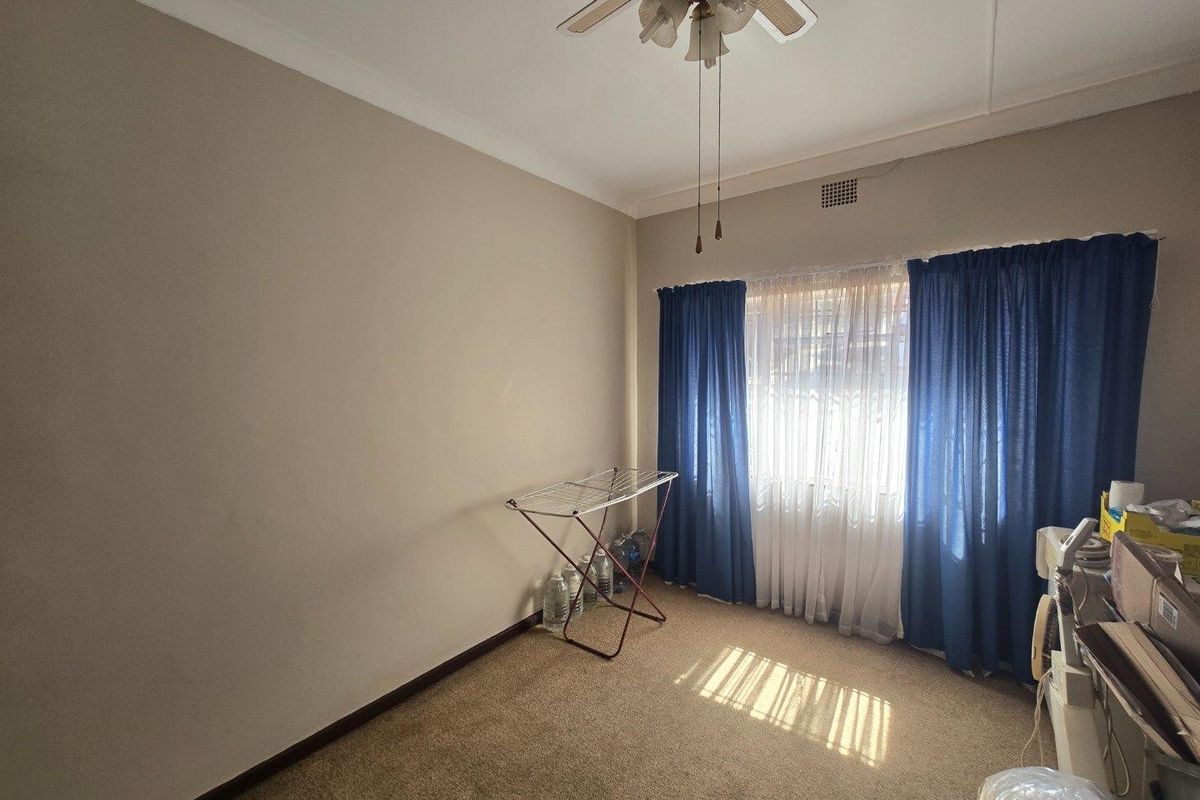 A vacant bedroom featuring carpeted flooring, a ceiling fan, and a window with curtain tracks.