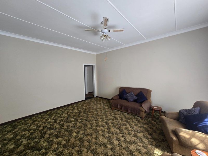 A living room featuring a ceiling fan and dated wall-to-wall carpeting, offering a blank canvas for modern updates and interior design improvements.