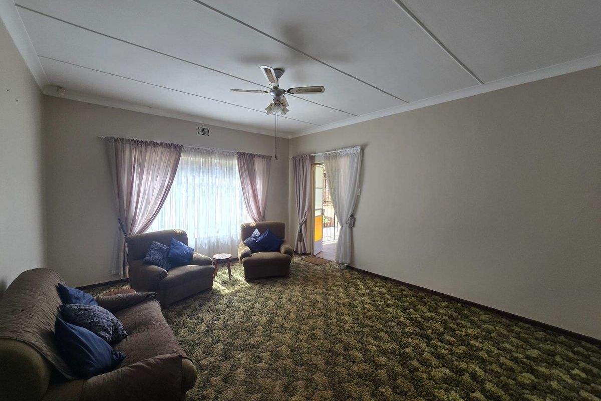 A spacious living room featuring a ceiling fan, large windows with curtains, and direct access to an outdoor area through a sliding door.