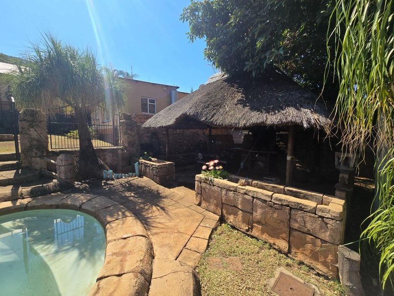 Outdoor pool area featuring a traditional thatch lapa, stone masonry walls, and paved surround, offering a rustic entertainment space.
