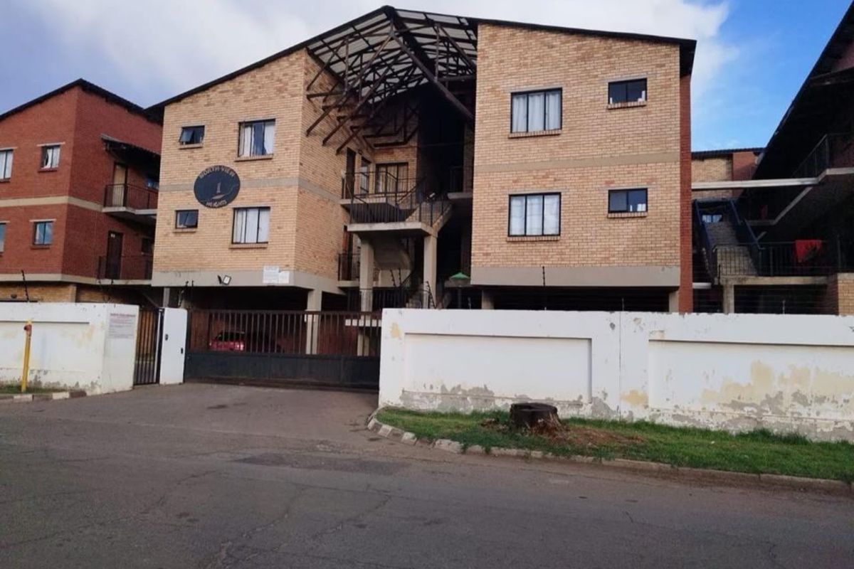 Front elevation of a multi-story apartment complex featuring face brick construction, secure gated access, and perimeter walling with electric fencing.