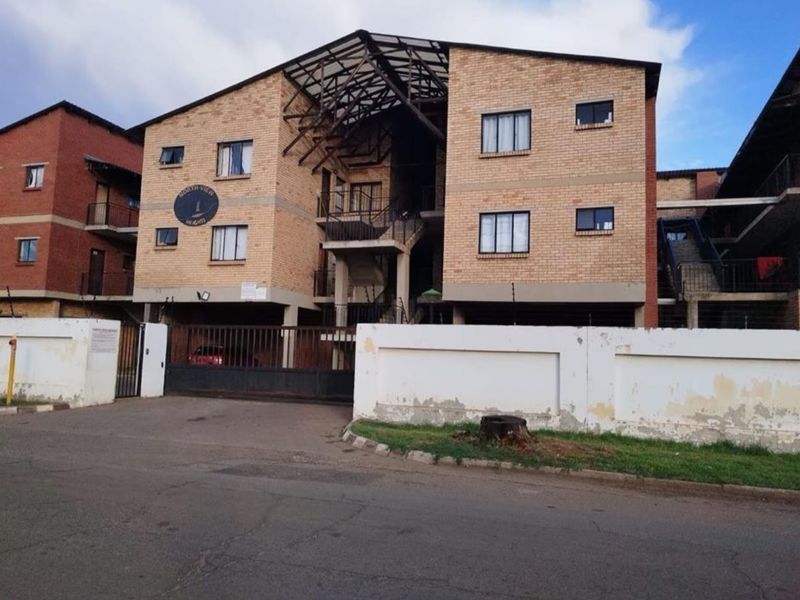 Front elevation of a multi-story apartment complex featuring face brick construction, secure gated access, and perimeter walling with electric fencing.
