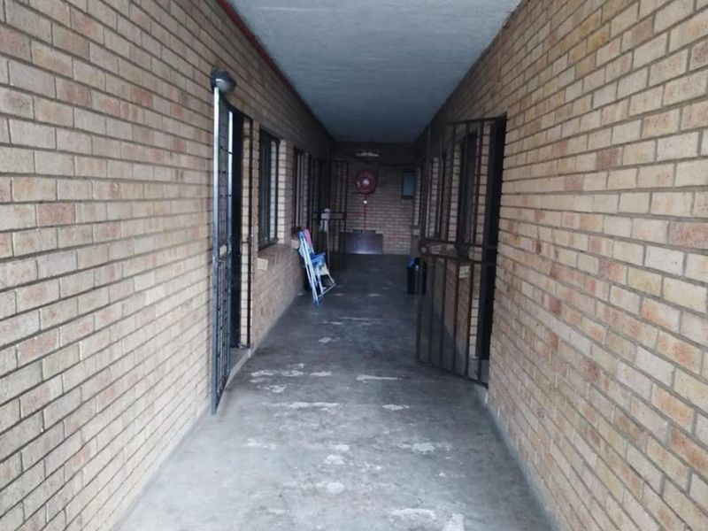 An exterior-facing apartment hallway featuring exposed brick walls, concrete flooring, and security gates providing access to individual units.
