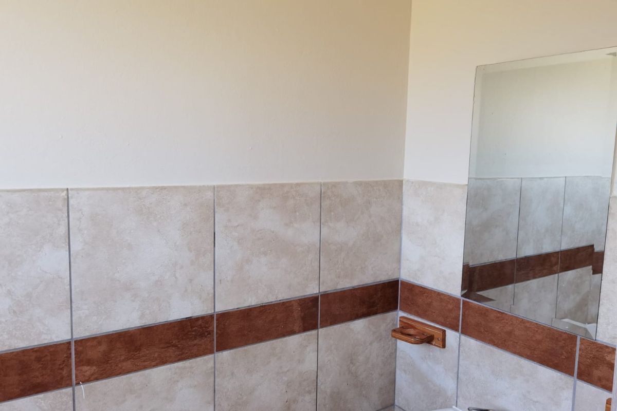 A bathroom featuring neutral ceramic wall tiles with a decorative accent border, a wall-mounted mirror, and a functional basin with a chrome faucet.
