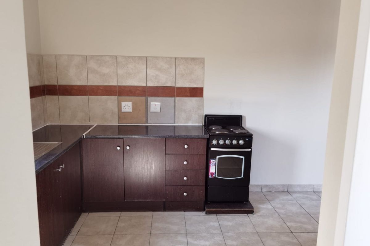 A functional kitchen featuring dark wood cabinetry, granite countertops, a tiled backsplash, and a freestanding electric stove with ceramic floor tiles.