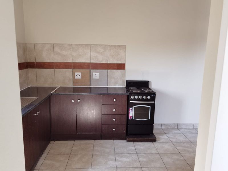 A functional kitchen featuring dark wood cabinetry, granite countertops, a tiled backsplash, and a freestanding electric stove with ceramic floor tiles.