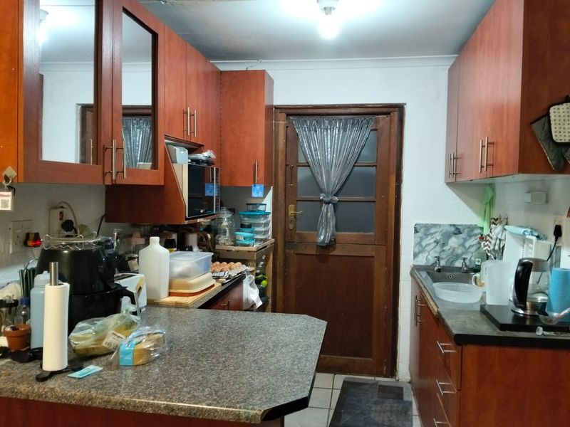 A compact kitchen featuring wood-tone cabinetry, laminate countertops, and a rear timber door, offering a functional layout with potential for modern updates.