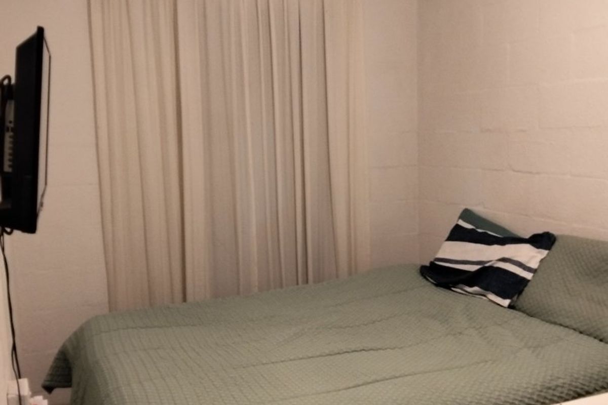 A simple bedroom featuring white painted brick walls, a coved ceiling, and a curtain rod installed over the window area.