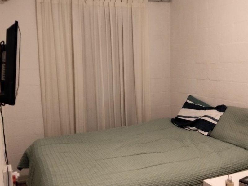 A simple bedroom featuring white painted brick walls, a coved ceiling, and a curtain rod installed over the window area.