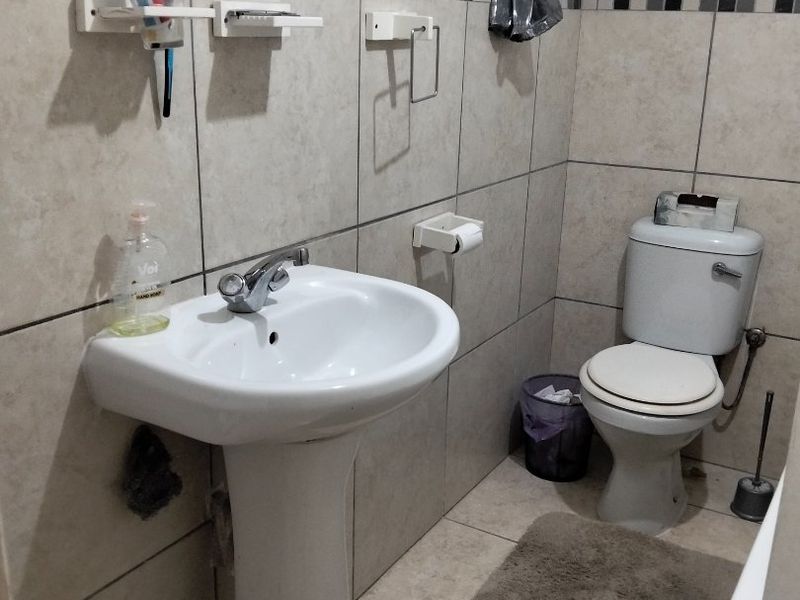 A functional bathroom featuring a pedestal washbasin, ceramic wall and floor tiling, and a standard toilet suite.