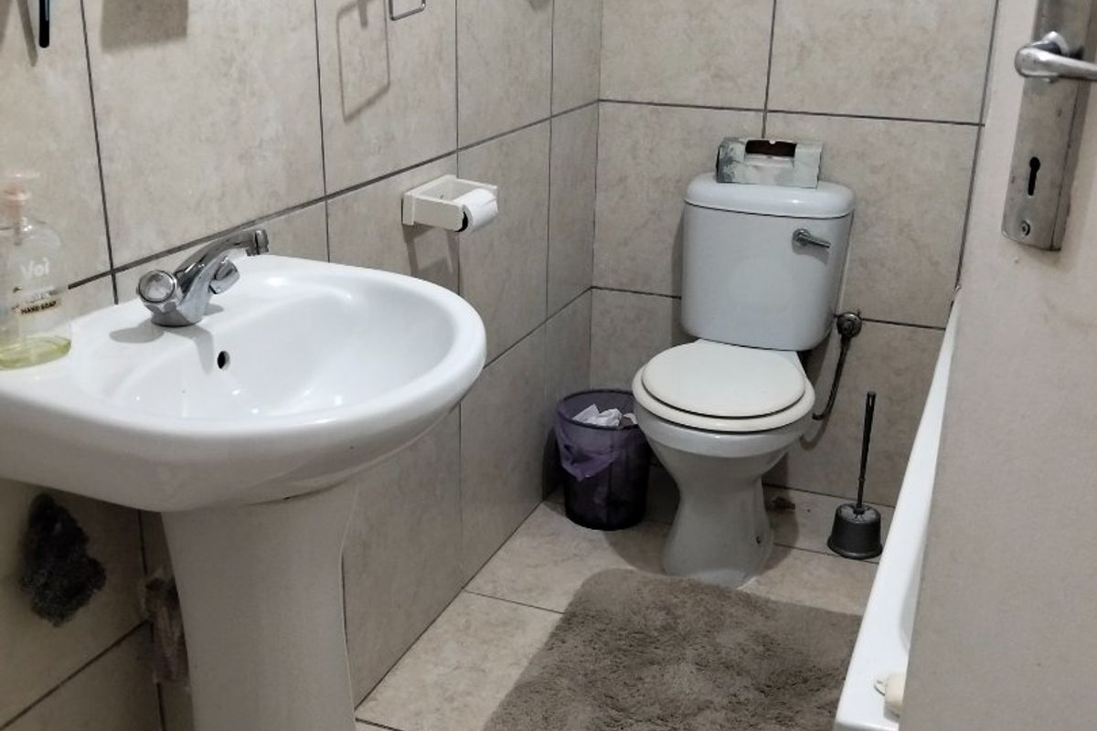 A functional bathroom featuring a pedestal basin, toilet, and neutral wall and floor tiling.