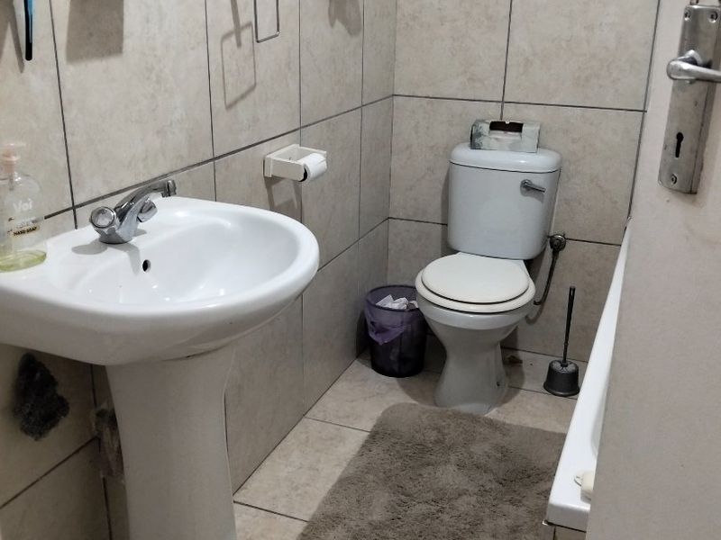 A functional bathroom featuring a pedestal basin, toilet, and neutral wall and floor tiling.