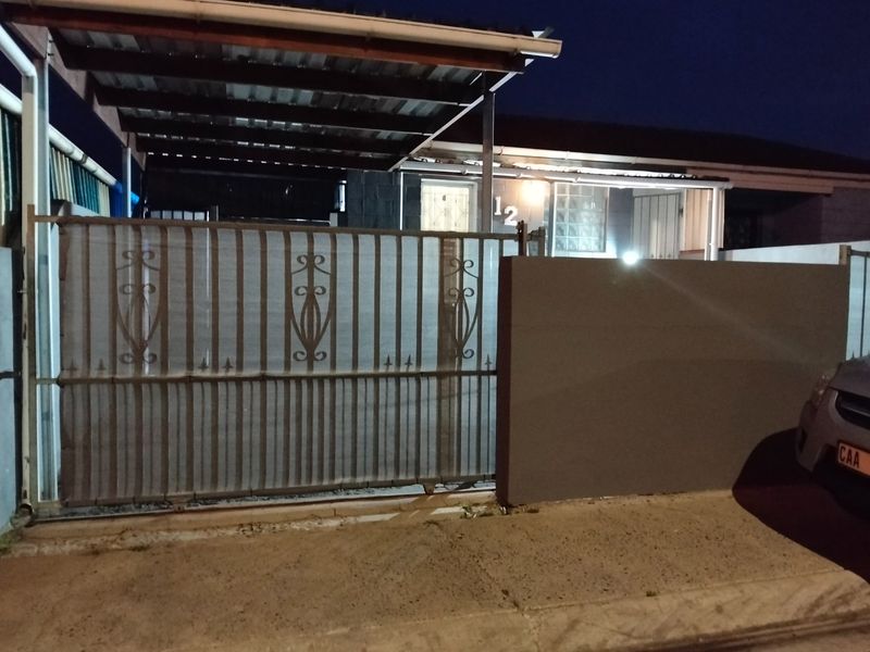 Front exterior view of the property featuring a metal sliding gate, covered carport, and boundary wall at night.