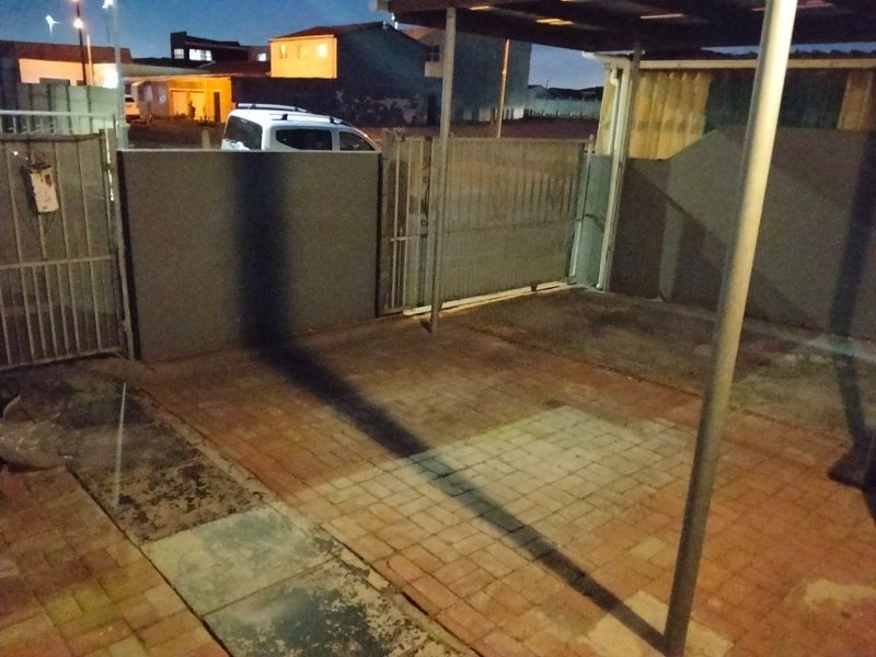 An outdoor carport area featuring paved flooring and metal security gates, providing covered parking space.