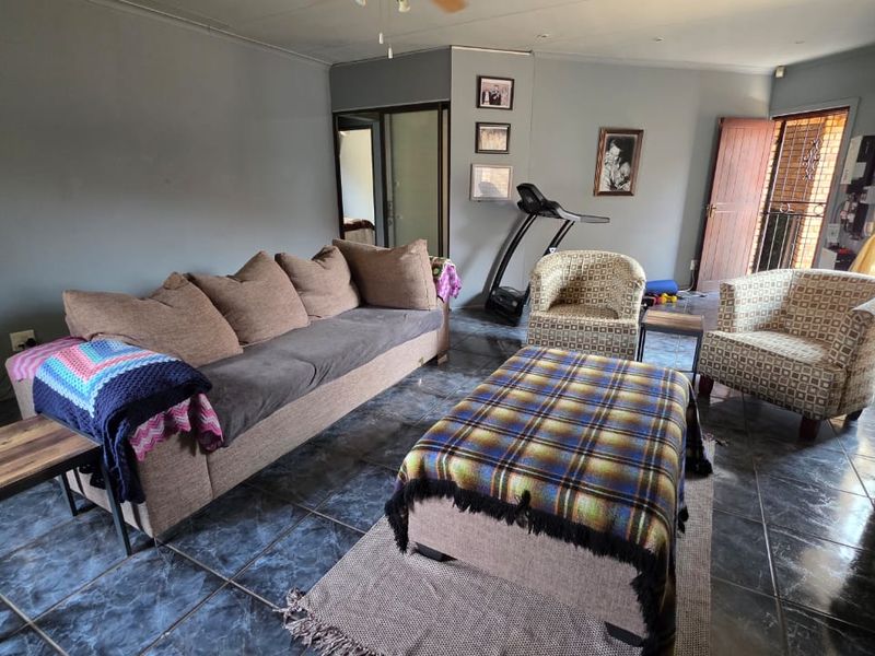 A living room featuring dark tiled flooring, a ceiling fan, and access to an exterior door.