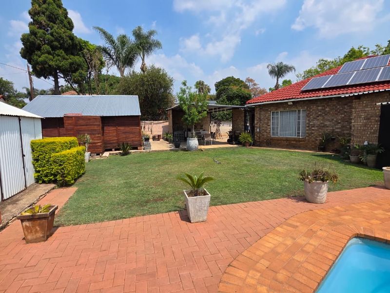 Spacious rear garden featuring a swimming pool, brick paved patio, solar panels on the roof, and a detached metal storage shed.