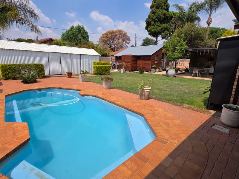 Spacious backyard featuring a swimming pool with brick paving, a well-maintained lawn, a corrugated metal storage shed, and a separate timber cabin.