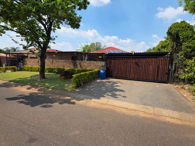 Front exterior view of the property featuring a paved driveway, secure timber gate, brick boundary wall, and solar panels installed on the tiled roof.