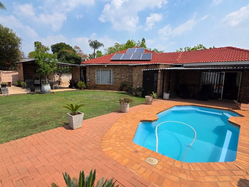 Rear view of the property featuring a swimming pool, brick paved patio area, and a face brick house with roof-mounted solar panels.