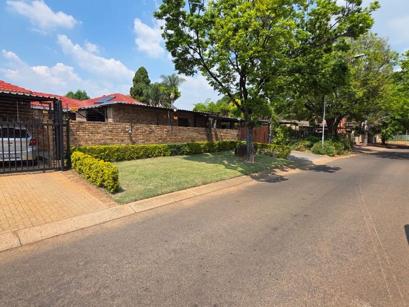 Street view of a residential property featuring a brick boundary wall, paved driveway, and well-maintained garden verge.