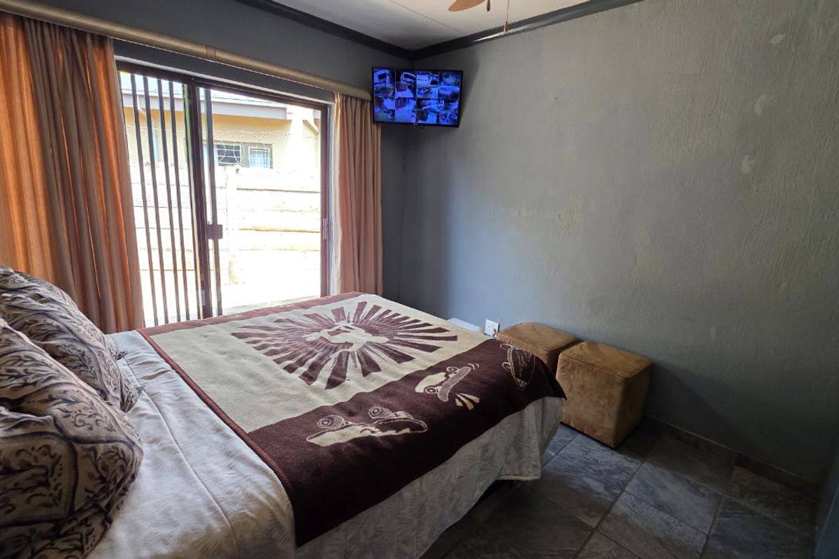 A bedroom featuring tiled flooring and a sliding glass door providing access to the exterior, with a ceiling fan and wall-mounted security monitor.