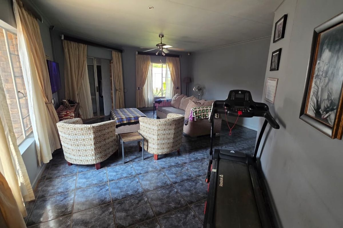 A spacious living room featuring dark tiled flooring, a ceiling fan, and large windows with sliding door access to the exterior.
