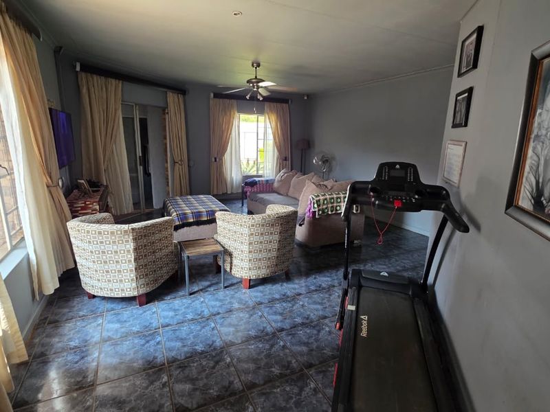 A spacious living room featuring dark tiled flooring, a ceiling fan, and large windows with sliding door access to the exterior.