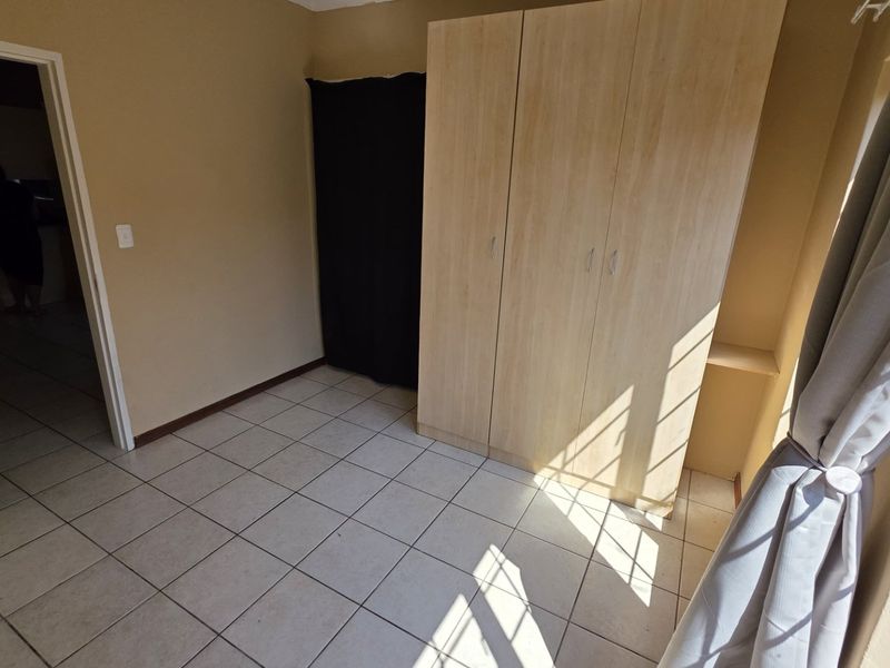 A simple bedroom featuring neutral tiled flooring and a built-in wooden wardrobe, offering a clean and functional space.