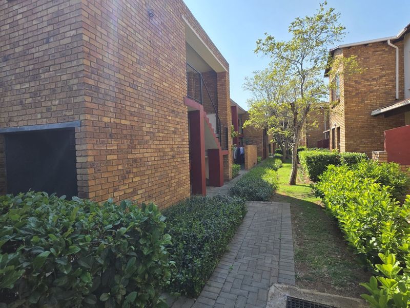 Exterior view of an apartment complex featuring face brick facades, a paved walkway, and established garden landscaping between the residential buildings.
