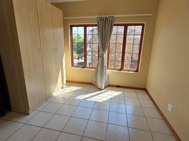 A bright, empty bedroom featuring tiled flooring, built-in cupboards, and a window with security bars, offering a clean and functional space.
