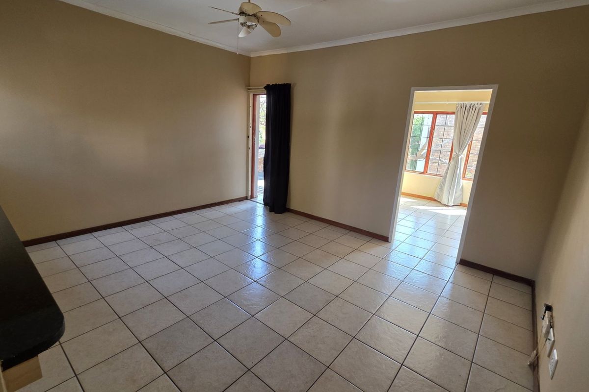 An empty living room featuring neutral tiled flooring, a ceiling fan, and direct access to an adjoining room and outdoor area.